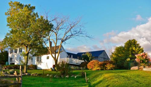 A picturesque scene of a white house and barn surrounded by trees and colorful foliage under a blue sky.