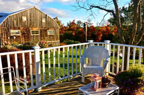 A cozy porch with a white chair and lantern, overlooking a lush green yard and a rustic barn surrounded by autumn foliage.