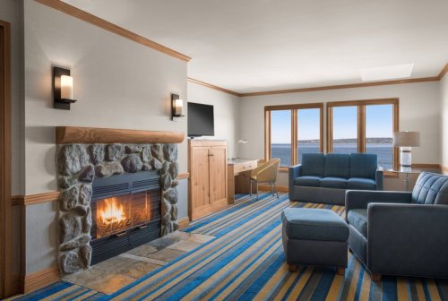 Cozy hotel room with a stone fireplace, blue furniture, and large windows overlooking a scenic view.