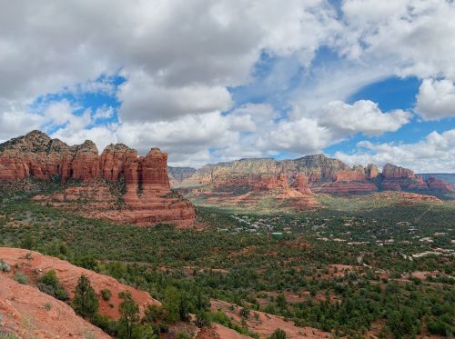 A panoramic view of red rock formations and green trees under a partly cloudy sky in Sedona, Arizona.