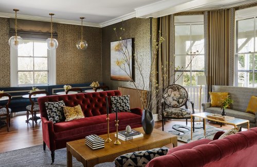 A stylish living room featuring a red tufted sofa, elegant decor, and large windows with natural light.