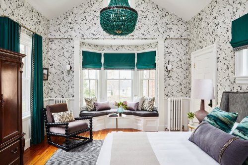 Brightly decorated bedroom featuring floral wallpaper, a green chandelier, and a cozy window seat with cushions.