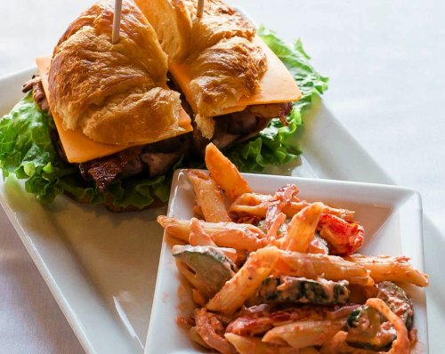 A croissant sandwich with cheese and lettuce, served with a side of creamy pasta salad.