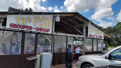 A seafood restaurant with outdoor seating, featuring signs for "The Fish" and "Mullet & More" under a blue sky.