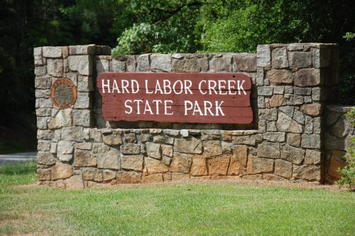 Sign for Hard Labor Creek State Park, featuring a stone structure and green surroundings.