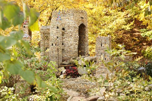 A miniature stone castle surrounded by greenery and autumn foliage.