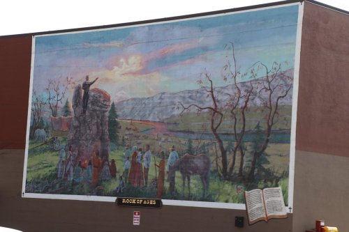 A mural depicting a scenic landscape with a figure on a rock, surrounded by people and a horse, under a colorful sky.