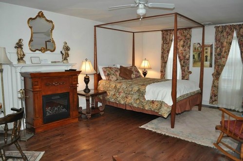 Cozy bedroom with a four-poster bed, floral curtains, a fireplace, and elegant decor.