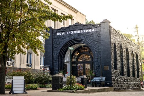 Historic black stone building with "Tug Valley Chamber of Commerce" sign, surrounded by greenery and a bench.