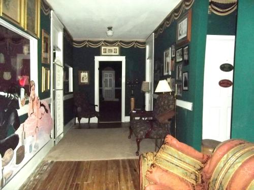 A dimly lit hallway with green walls, framed pictures, and vintage furniture, leading to a door at the end.