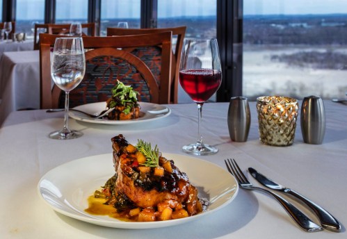 A beautifully plated dish with meat and vegetables, accompanied by glasses of water and red wine, in an elegant dining setting.