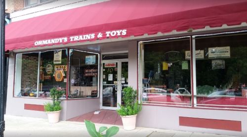 Exterior of Ormandy's Trains & Toys store, featuring a red awning and large windows displaying toys and model trains.