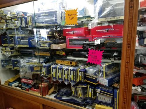 A display case filled with various model trains and accessories, mostly in blue and yellow packaging.