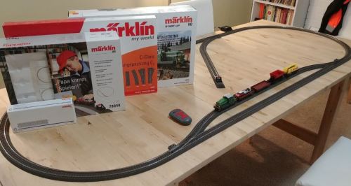 A model train set on a wooden table, featuring tracks, a train, and packaging from Märklin.