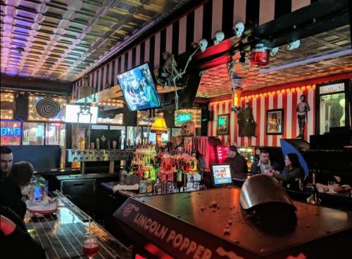 A vibrant bar scene with colorful decor, shelves of liquor, and a vintage atmosphere featuring skulls and eclectic lighting.