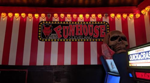 A vibrant wall with red and white stripes, featuring a "Funhouse Cleveland" sign, skull decorations, and an arcade machine.