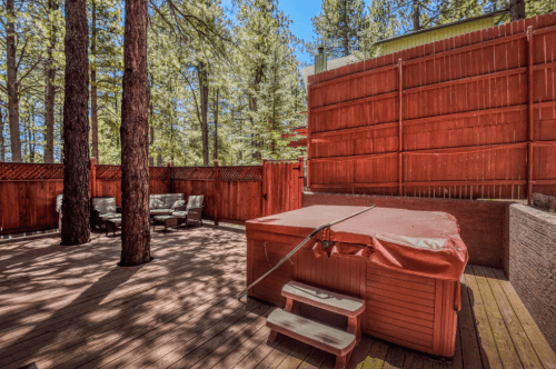 A wooden deck surrounded by trees, featuring a hot tub and outdoor seating area.