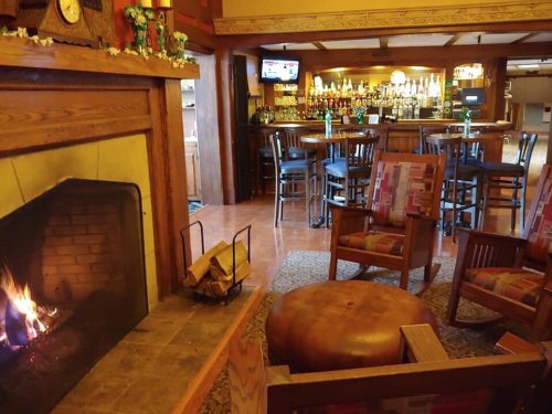 Cozy interior of a bar with a fireplace, wooden furniture, and a well-stocked bar in the background.
