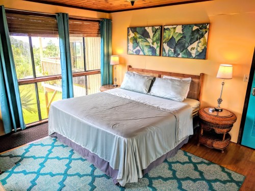Cozy bedroom with a large bed, tropical decor, and windows overlooking a lush outdoor view.