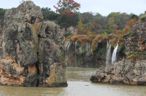 A serene landscape featuring rocky formations and a waterfall cascading into a calm body of water, surrounded by autumn foliage.