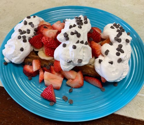 A blue plate with sliced strawberries, bananas, whipped cream, and chocolate chips arranged on top.