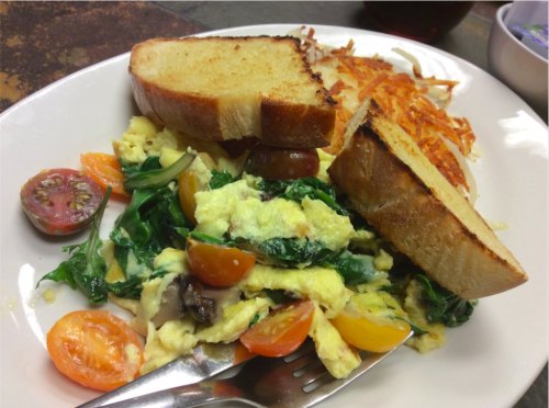 A plate with scrambled eggs, spinach, cherry tomatoes, hash browns, and two slices of toasted bread.