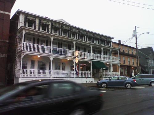 A historic white building with multiple balconies, a green awning, and parked cars in front on a cloudy day.
