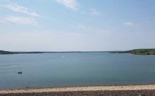 A serene lake view with a clear blue sky, gentle waves, and a small boat on the water, surrounded by green hills.