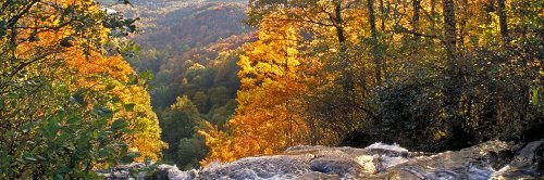 A scenic view of a waterfall surrounded by vibrant autumn foliage and rolling hills in the background.