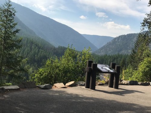 A scenic view of mountains and forests, with a wooden information sign in the foreground.