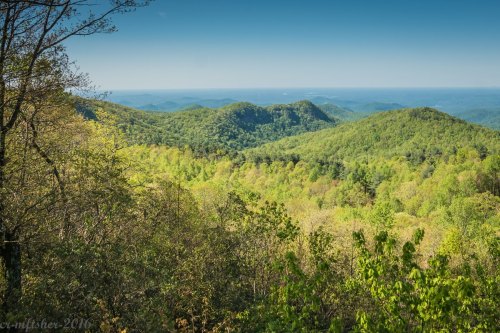 Lush green mountains stretch into the distance under a clear blue sky, showcasing a serene natural landscape.