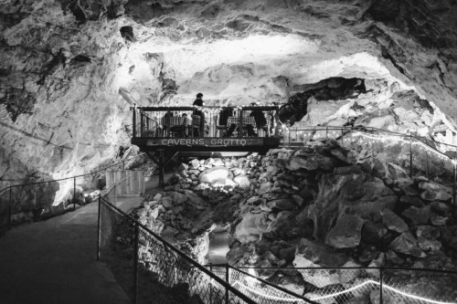 A black and white image of a cave interior with a viewing platform and rocky formations illuminated by soft lights.