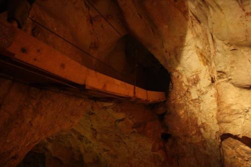 A dimly lit cave interior featuring a wooden walkway suspended above rocky terrain.