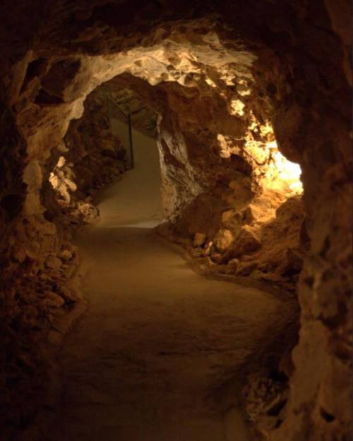 A dimly lit cave pathway with rocky walls and a smooth, winding floor.