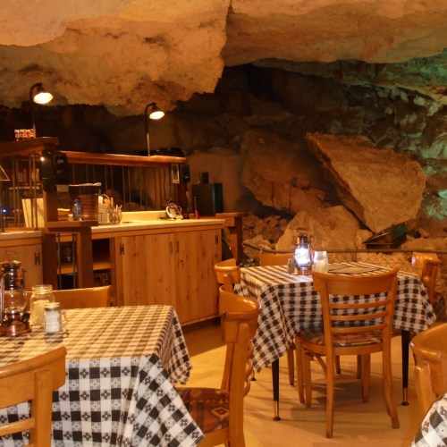 A cozy cave restaurant with wooden tables, checkered tablecloths, and rock formations in the background.