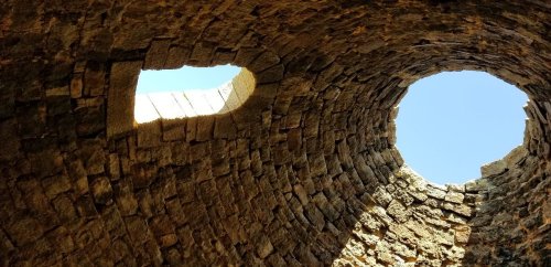 View looking up at a stone structure with two circular openings letting in light from above.