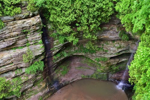 A serene natural scene featuring a rocky cliff with lush greenery and a small waterfall flowing into a calm pool below.