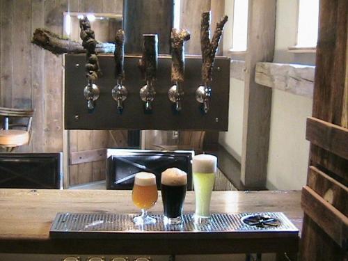A rustic bar with four beer taps and three glasses of beer: a dark stout, a light lager, and a golden ale.