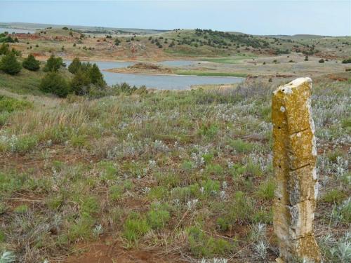 A rocky outcrop stands in the foreground, overlooking a serene lake surrounded by rolling hills and greenery.