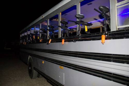 A modified bus at night, equipped with paintball guns mounted along the side. Blue lights illuminate the interior.