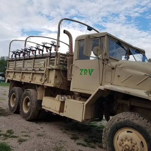 A military-style truck with a green "ZRV" marking, equipped with multiple mounted tools, parked on a gravel surface.