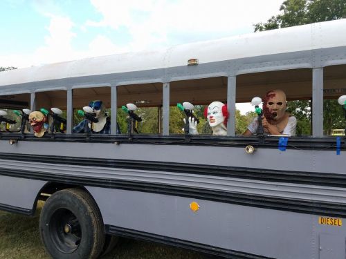 A school bus with creepy masks and props displayed in the windows, set against a grassy background.