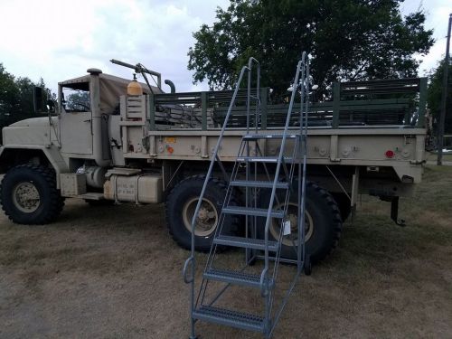 A military truck parked on grass, with a metal staircase leading up to its flatbed.