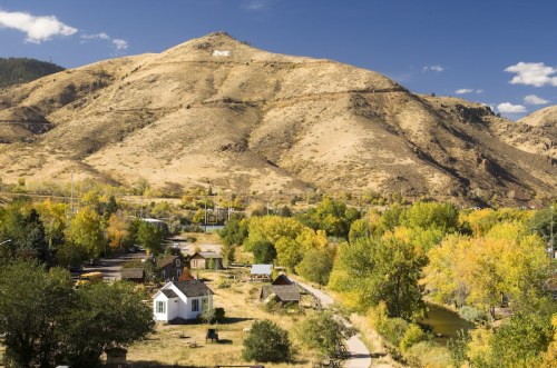 A scenic view of a hillside with a large letter "M," surrounded by autumn-colored trees and a small village below.