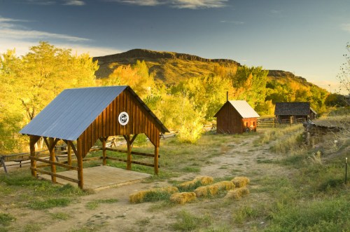A rustic landscape featuring wooden structures, surrounded by vibrant autumn foliage and a distant mountain backdrop.