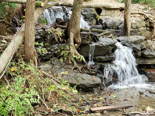 A serene waterfall cascades over rocks, surrounded by trees and lush greenery in a peaceful natural setting.