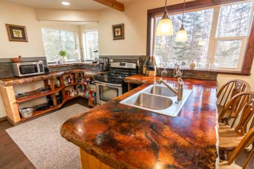 Cozy kitchen with wooden countertops, modern appliances, and large windows overlooking a forested area.