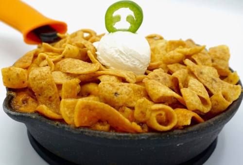 A skillet filled with Fritos topped with a dollop of sour cream and a slice of jalapeño.