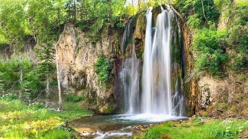 A serene waterfall cascading over rocky cliffs, surrounded by lush greenery and a tranquil pool below.