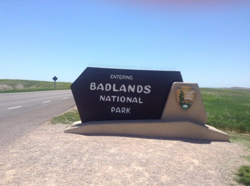 Sign marking the entrance to Badlands National Park, with clear blue skies and green grass in the background.